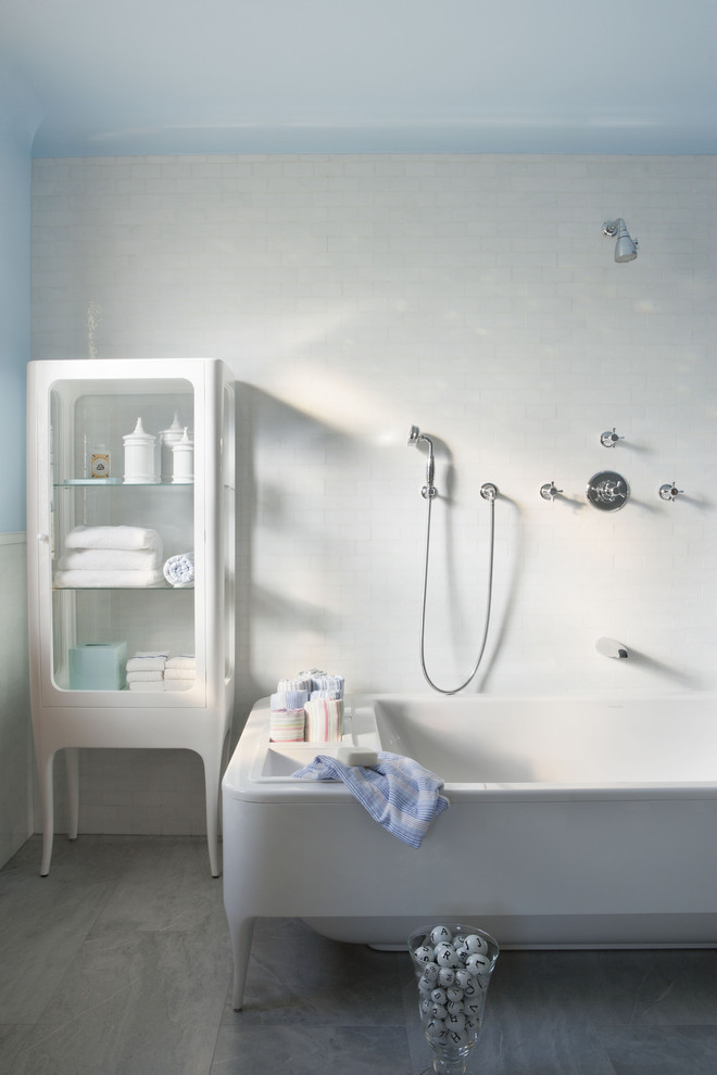 ニューヨークにあるモダンスタイルのおしゃれな浴室 (置き型浴槽、白いキャビネット、シャワー付き浴槽	、白いタイル、グレーの床) の写真