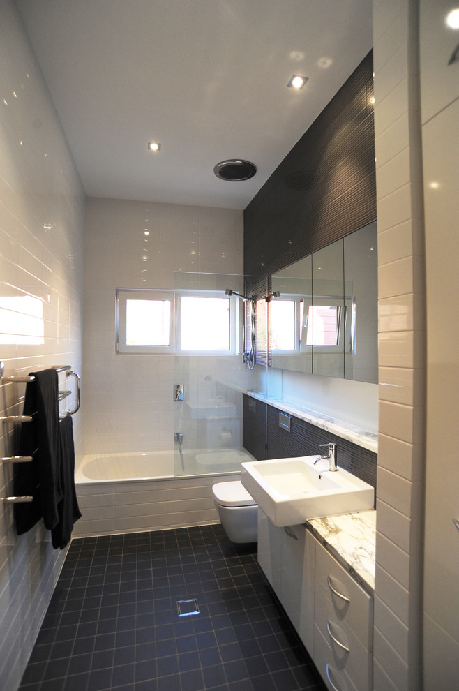 Cette image montre une petite salle de bain design avec un plan de toilette en marbre, une baignoire posée, un combiné douche/baignoire, WC suspendus, un carrelage gris et un mur blanc.