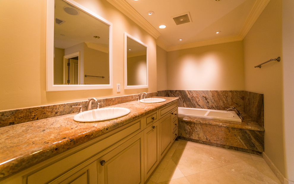 Expansive mediterranean ensuite bathroom in San Diego with a built-in sink, beaded cabinets, beige cabinets, granite worktops, an alcove bath, an alcove shower, a one-piece toilet, beige tiles, stone tiles, beige walls and marble flooring.