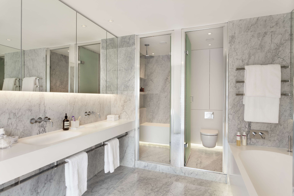 Design ideas for a medium sized contemporary ensuite bathroom in London with white cabinets, an alcove shower, a wall mounted toilet, grey tiles, white walls, ceramic flooring, a built-in sink, quartz worktops, grey floors, a hinged door, white worktops, an enclosed toilet, a single sink and a built in vanity unit.