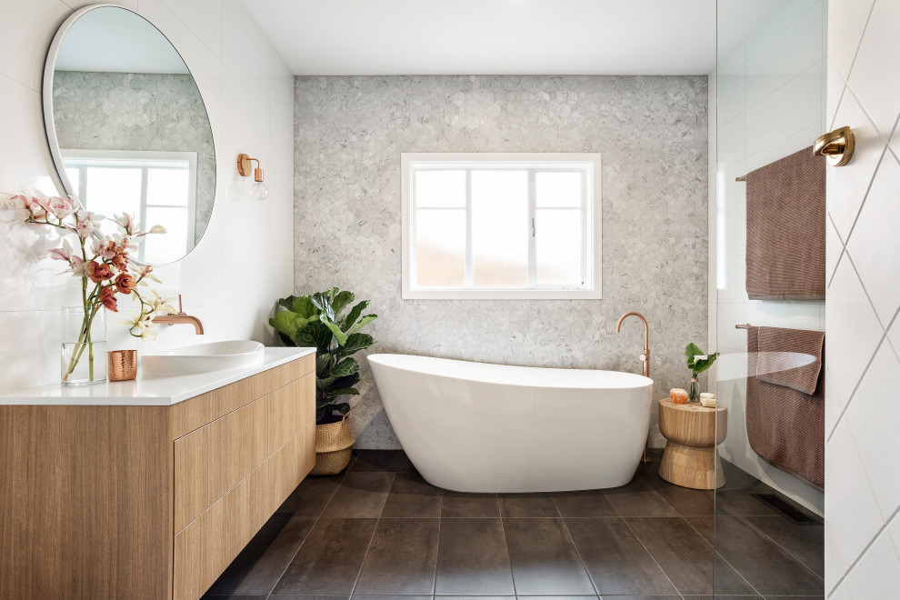 Cette image montre une salle de bain principale design en bois clair avec un placard à porte plane, une baignoire indépendante, un carrelage gris, une vasque, un sol gris, un plan de toilette blanc, meuble simple vasque et meuble-lavabo suspendu.