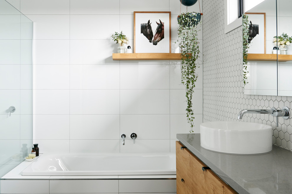 Cette image montre une salle de bain principale design en bois brun avec un placard à porte plane, une baignoire d'angle, un carrelage blanc, des carreaux de céramique, un mur blanc, une vasque et un plan de toilette en béton.