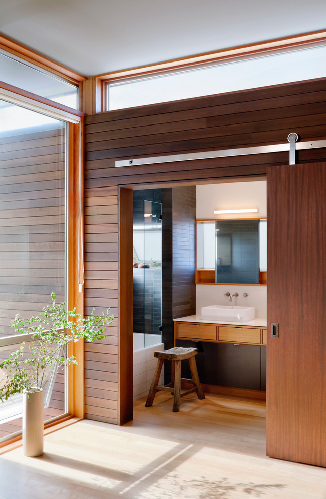 Idées déco pour une salle de bain contemporaine en bois clair avec une vasque, un placard à porte plane et un combiné douche/baignoire.