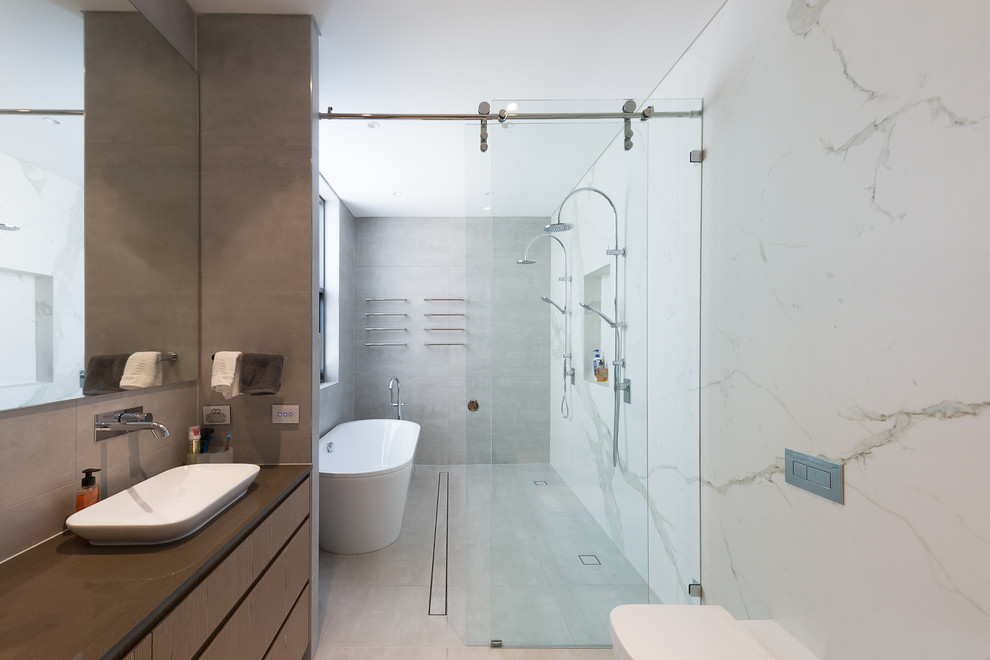 Пример оригинального дизайна: большая ванная комната в современном стиле с плоскими фасадами, фасадами цвета дерева среднего тона, отдельно стоящей ванной, душевой комнатой, белой плиткой, плиткой из листового камня, настольной раковиной, серым полом и серой столешницей