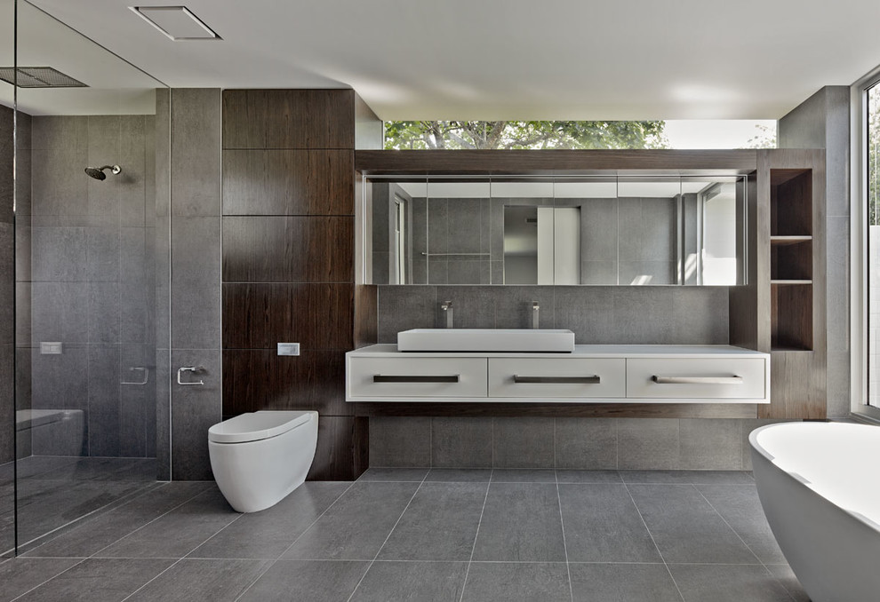 Идея дизайна: главная ванная комната в стиле модернизм с темными деревянными фасадами, отдельно стоящей ванной, душем без бортиков, инсталляцией, серой плиткой, раковиной с несколькими смесителями и коричневыми стенами