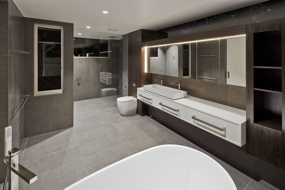 Idéer för ett modernt en-suite badrum, med skåp i mörkt trä, ett fristående badkar, en kantlös dusch, en vägghängd toalettstol, grå kakel och grå väggar