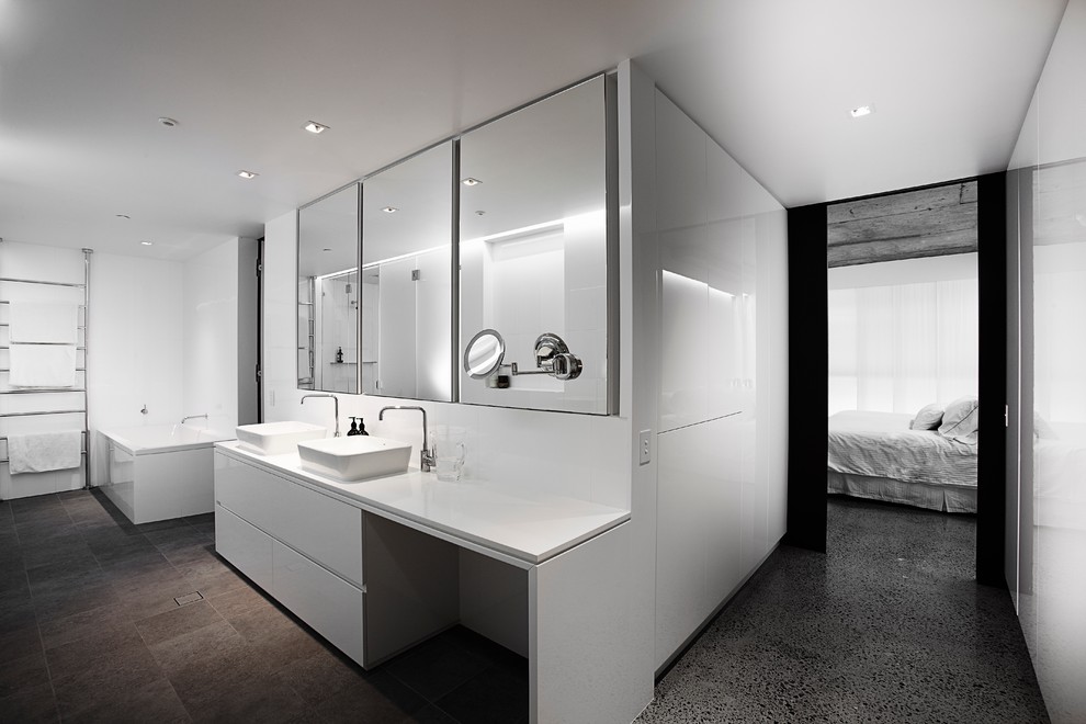 Modelo de cuarto de baño actual con lavabo sobreencimera, armarios con paneles lisos, puertas de armario blancas y paredes blancas