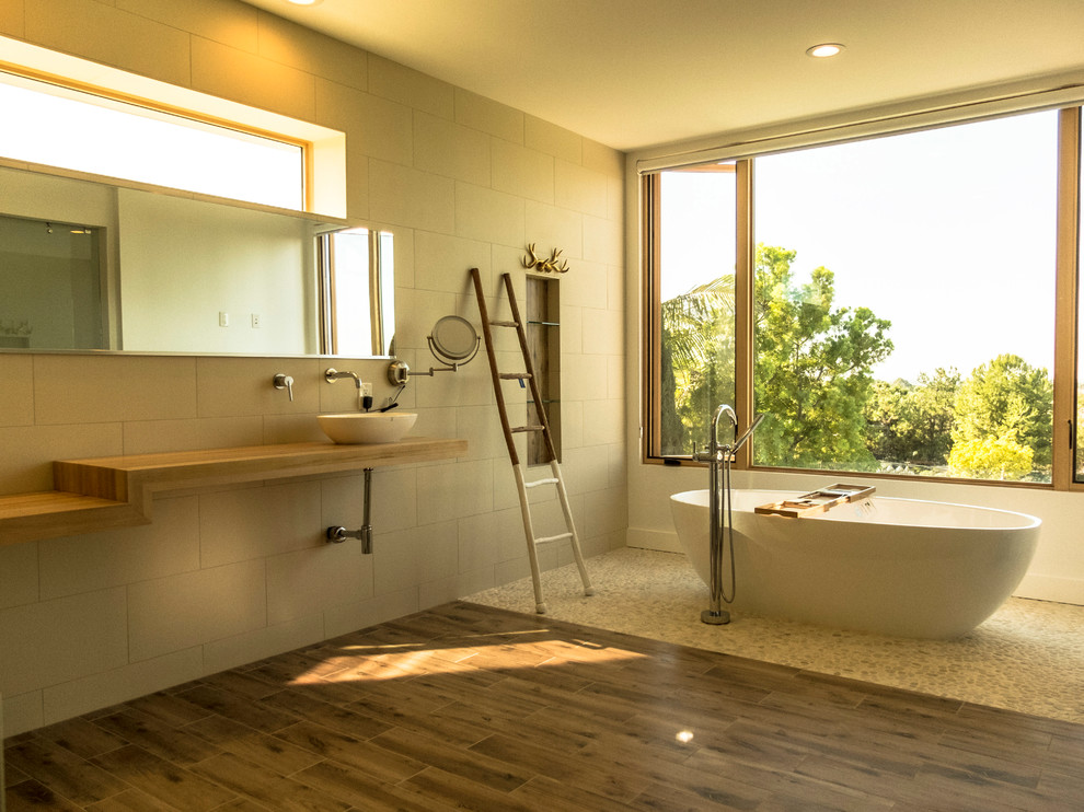 Cette image montre une très grande douche en alcôve principale minimaliste avec une baignoire indépendante, un mur blanc, un placard sans porte, un carrelage gris, une plaque de galets, un sol en carrelage de porcelaine, une vasque et un plan de toilette en bois.