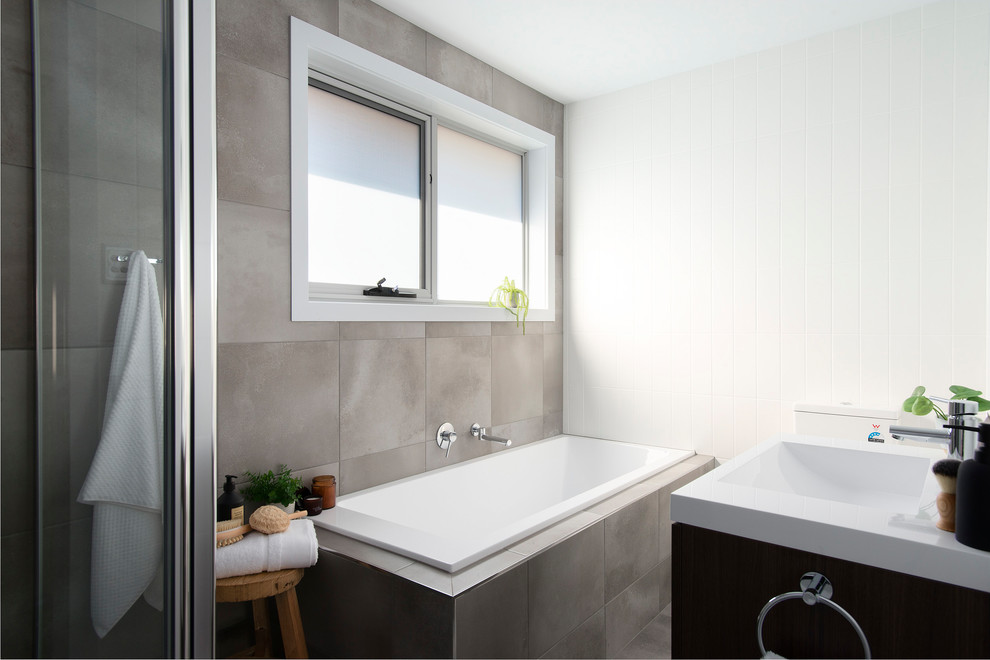 Design ideas for a small contemporary ensuite bathroom in Other with recessed-panel cabinets, dark wood cabinets, a built-in bath, a corner shower, a one-piece toilet, white tiles, ceramic tiles, grey walls, cement flooring, a wall-mounted sink, solid surface worktops, grey floors, a hinged door and white worktops.