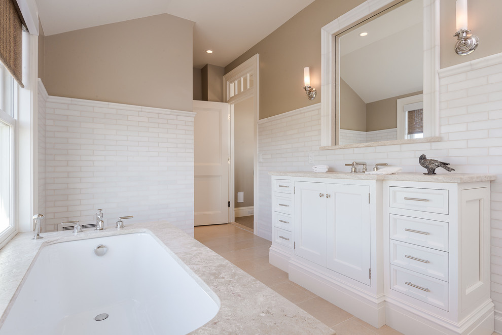 Cette image montre une salle de bain marine avec un lavabo encastré, un placard en trompe-l'oeil, des portes de placard blanches, une baignoire encastrée, un carrelage blanc, un carrelage de pierre et un mur beige.