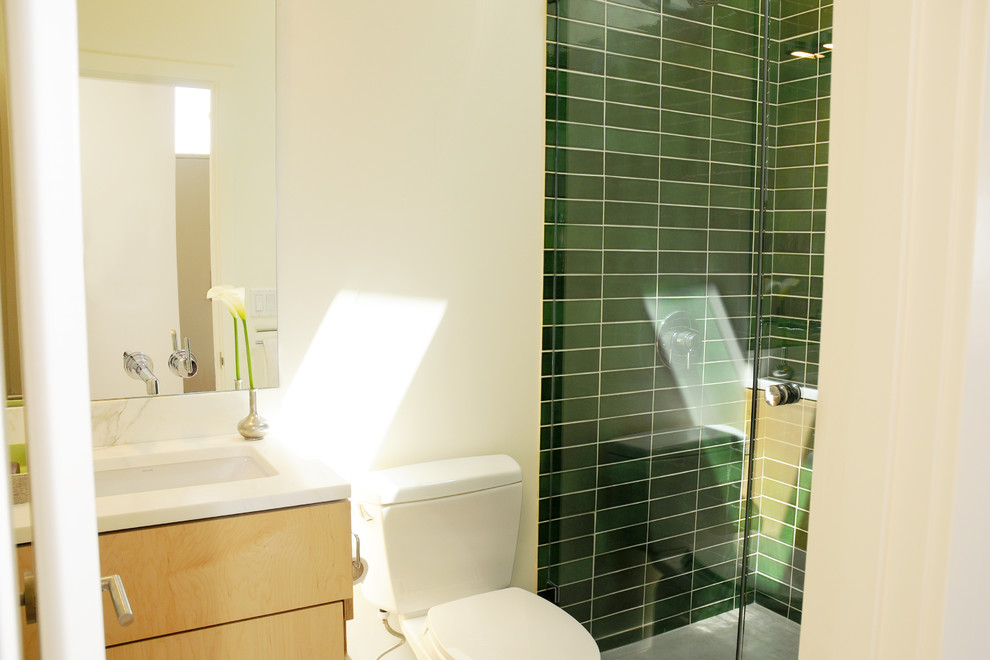 Immagine di una stanza da bagno moderna con lavabo integrato, ante lisce, ante in legno chiaro, doccia ad angolo, WC a due pezzi, piastrelle verdi e piastrelle in ceramica