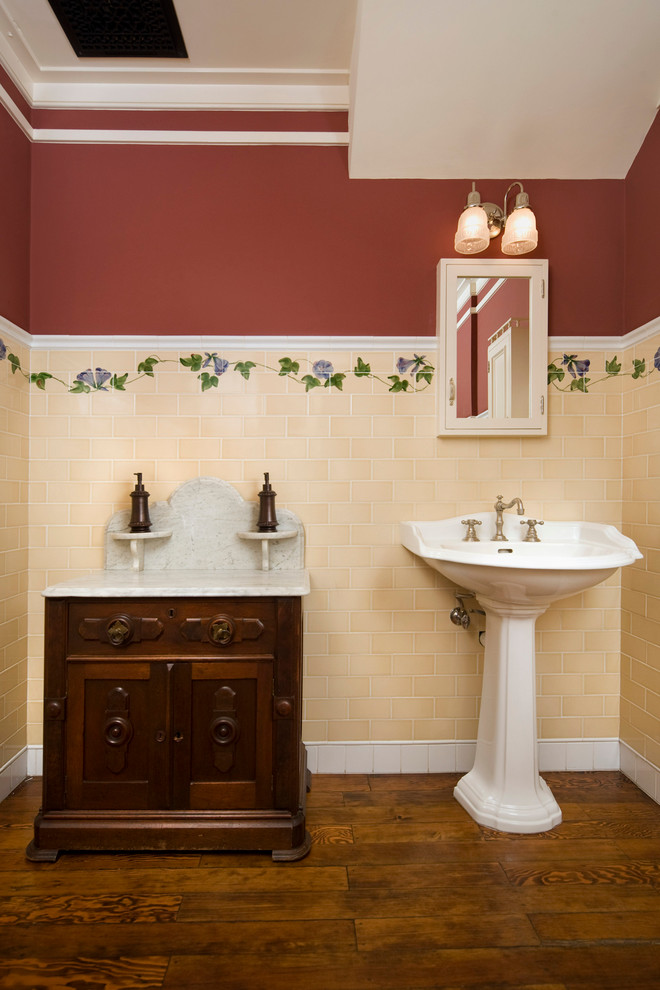 Immagine di una stanza da bagno classica con lavabo a colonna, piastrelle gialle, consolle stile comò, ante in legno bruno, top in marmo, piastrelle in ceramica, pareti marroni e parquet scuro