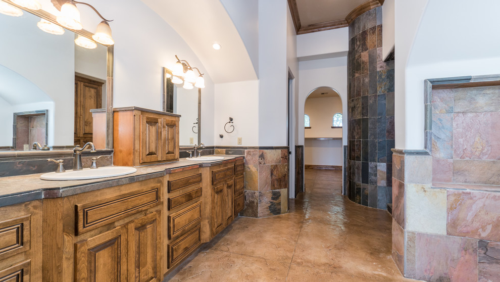 Cette image montre une grande salle de bain principale méditerranéenne en bois foncé avec un placard avec porte à panneau surélevé, un carrelage multicolore, un carrelage de pierre, un mur blanc, sol en béton ciré, un lavabo posé, un plan de toilette en carrelage et un sol marron.
