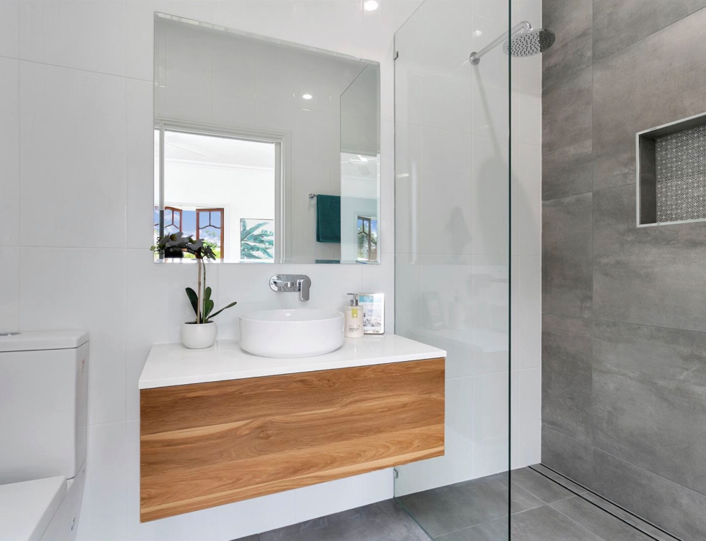 Idéer för att renovera ett mellanstort funkis vit vitt badrum med dusch, med släta luckor, skåp i mellenmörkt trä, en kantlös dusch, grå kakel, porslinskakel, klinkergolv i porslin, ett fristående handfat och grått golv