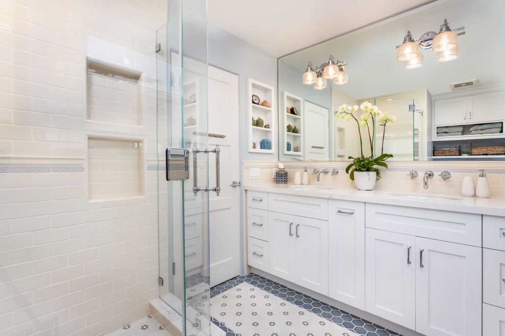 Пример оригинального дизайна: ванная комната среднего размера в стиле неоклассика (современная классика) с фасадами в стиле шейкер, белыми фасадами, угловым душем, бежевой плиткой, плиткой кабанчик, полом из мозаичной плитки, душевой кабиной, врезной раковиной, столешницей из искусственного кварца, разноцветным полом, душем с распашными дверями, белой столешницей, тумбой под две раковины, встроенной тумбой, серыми стенами и нишей