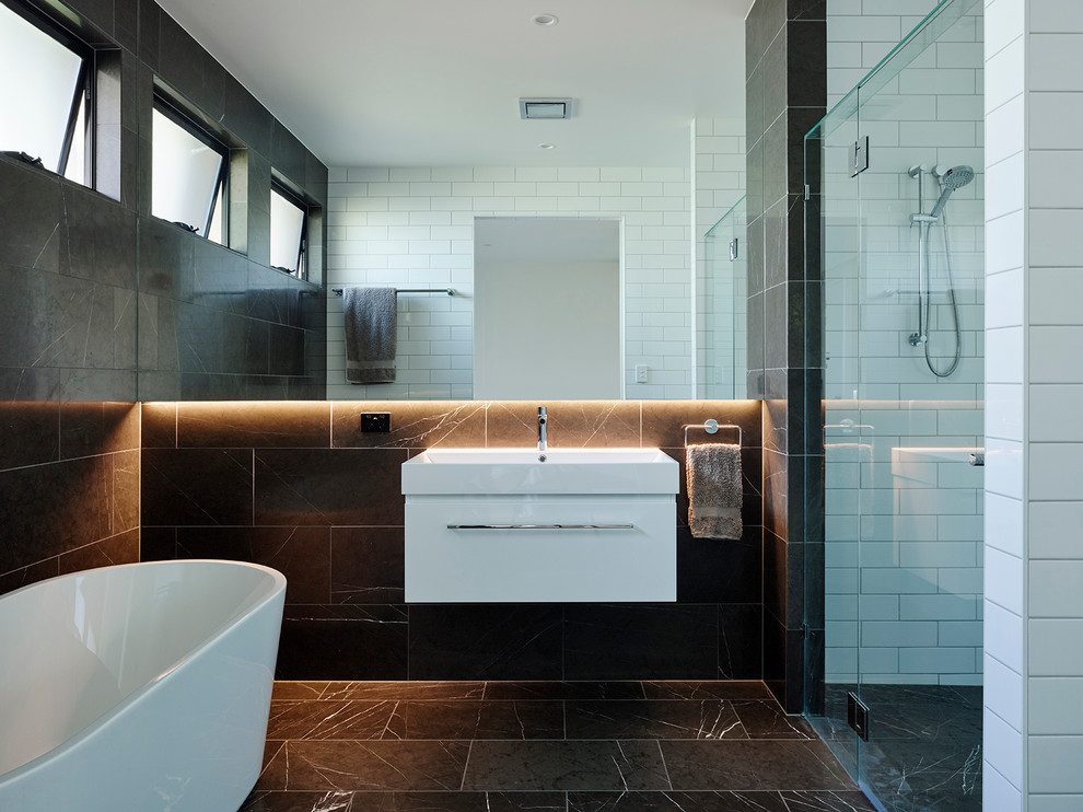 Inredning av ett maritimt badrum, med släta luckor, vita skåp, ett fristående badkar, en dusch i en alkov, svart kakel, svart och vit kakel, flerfärgade väggar, bambugolv och ett väggmonterat handfat