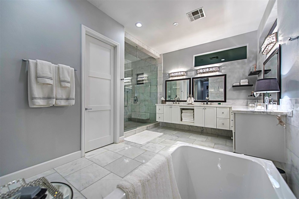 Пример оригинального дизайна: огромная главная ванная комната в современном стиле с фасадами в стиле шейкер, белыми фасадами, отдельно стоящей ванной, душем в нише, серой плиткой, белой плиткой, каменной плиткой, серыми стенами, мраморным полом, врезной раковиной и столешницей из гранита