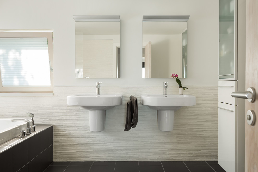 Foto di una stanza da bagno padronale design con lavabo sospeso, ante bianche, pavimento in gres porcellanato, vasca da incasso, piastrelle nere, pareti bianche e ante lisce