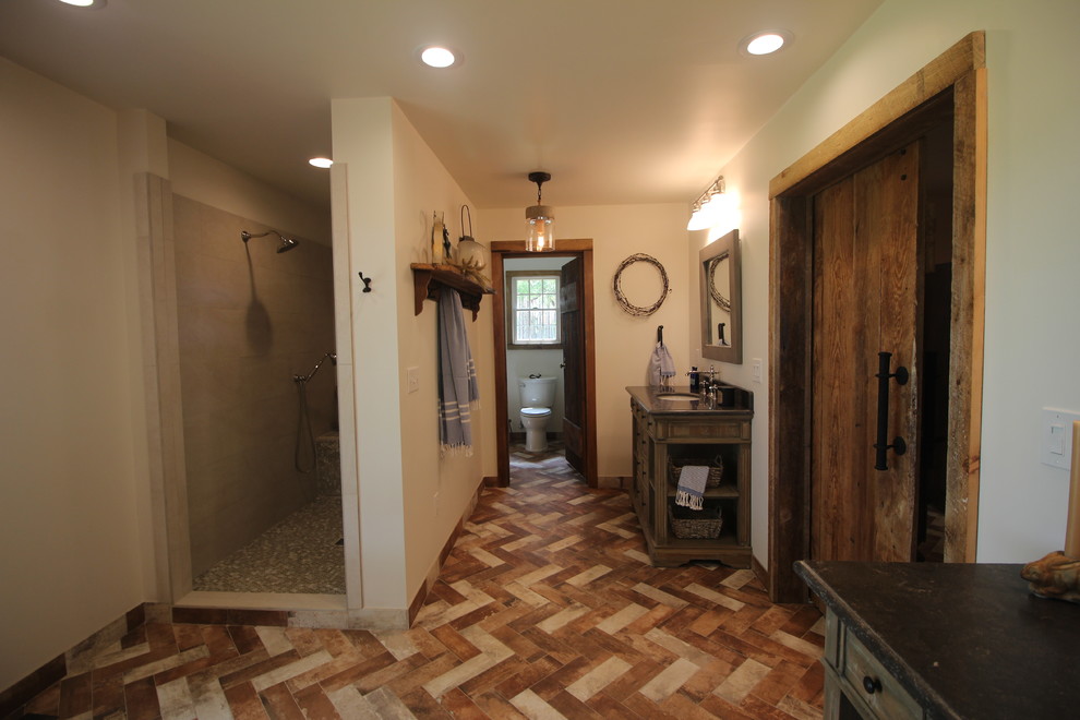 Medium sized rural ensuite bathroom in Atlanta with freestanding cabinets, distressed cabinets, a freestanding bath, a walk-in shower, a one-piece toilet, beige tiles, porcelain tiles, white walls, brick flooring, a submerged sink, soapstone worktops, multi-coloured floors, an open shower and grey worktops.