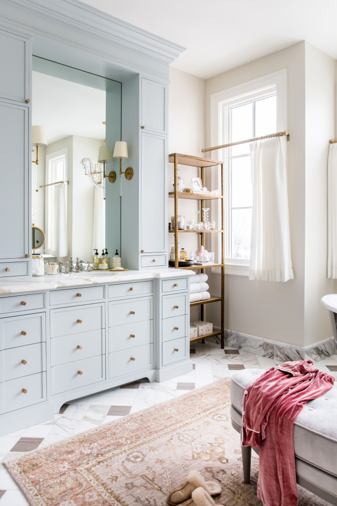Inredning av ett klassiskt stort vit vitt en-suite badrum, med blå skåp, ett fristående badkar, en dubbeldusch, en toalettstol med separat cisternkåpa, rosa väggar, ett undermonterad handfat, marmorbänkskiva, dusch med gångjärnsdörr, flerfärgat golv och luckor med profilerade fronter