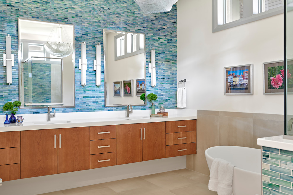 Cette photo montre une salle de bain tendance en bois brun avec un placard à porte plane, une baignoire indépendante, un carrelage bleu, un mur blanc, un lavabo encastré, un sol beige et un plan de toilette blanc.