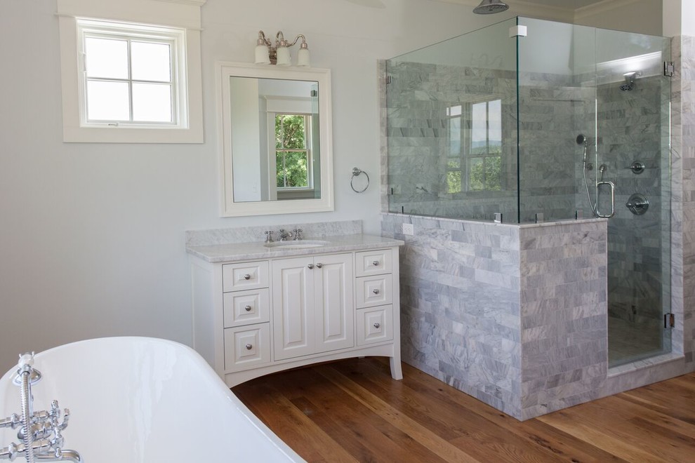 Exemple d'une grande salle de bain principale nature avec un placard avec porte à panneau surélevé, des portes de placard blanches, une baignoire indépendante, une douche d'angle, un carrelage gris, un carrelage blanc, un sol en bois brun, un lavabo encastré et un plan de toilette en marbre.