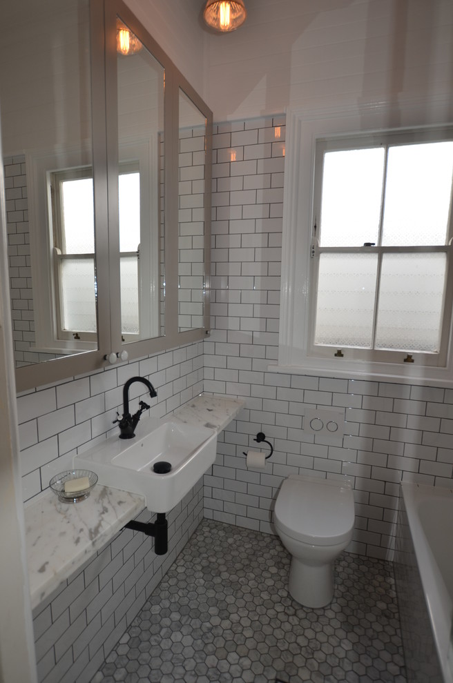 Klassisk inredning av ett badrum, med ett integrerad handfat, ett badkar i en alkov, en dusch/badkar-kombination, luckor med infälld panel, marmorbänkskiva, vit kakel och tunnelbanekakel