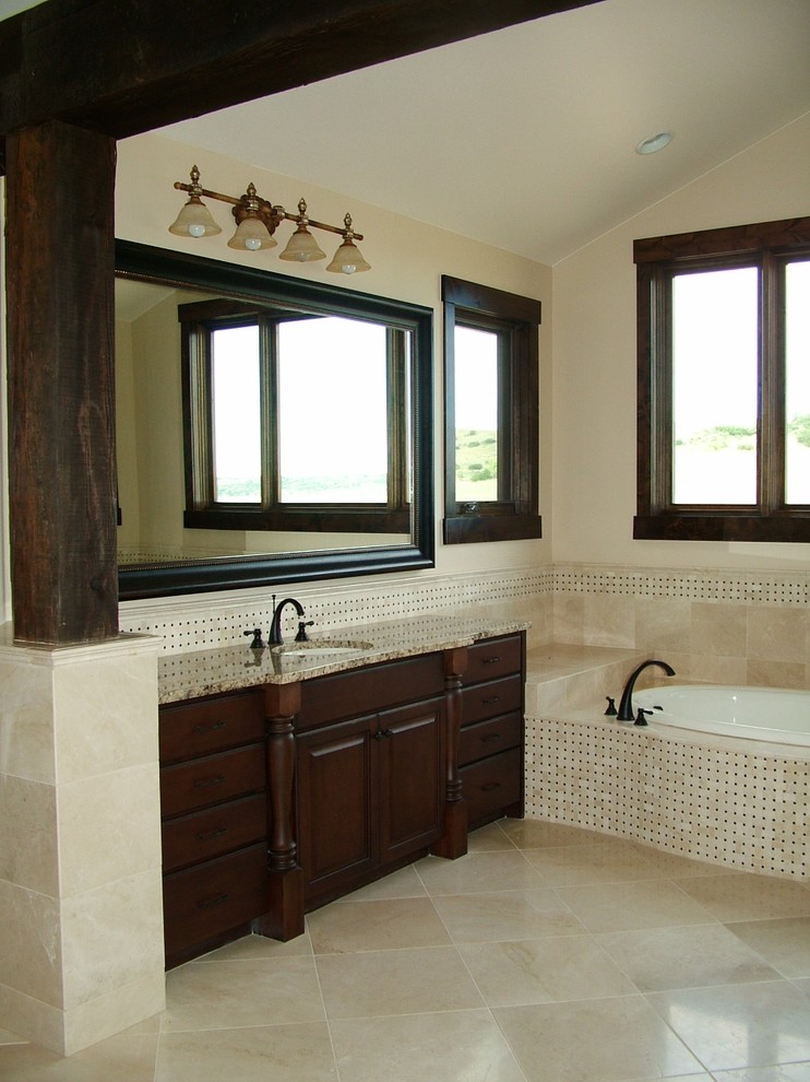 Photo of a classic bathroom in Denver with a submerged sink, dark wood cabinets, a built-in bath, beige tiles, raised-panel cabinets and feature lighting.