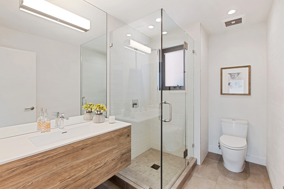 Mid-sized trendy 3/4 white tile and porcelain tile porcelain tile and brown floor corner shower photo in San Francisco with flat-panel cabinets, a one-piece toilet, white walls, an integrated sink, solid surface countertops, a hinged shower door, white countertops, a floating vanity and medium tone wood cabinets