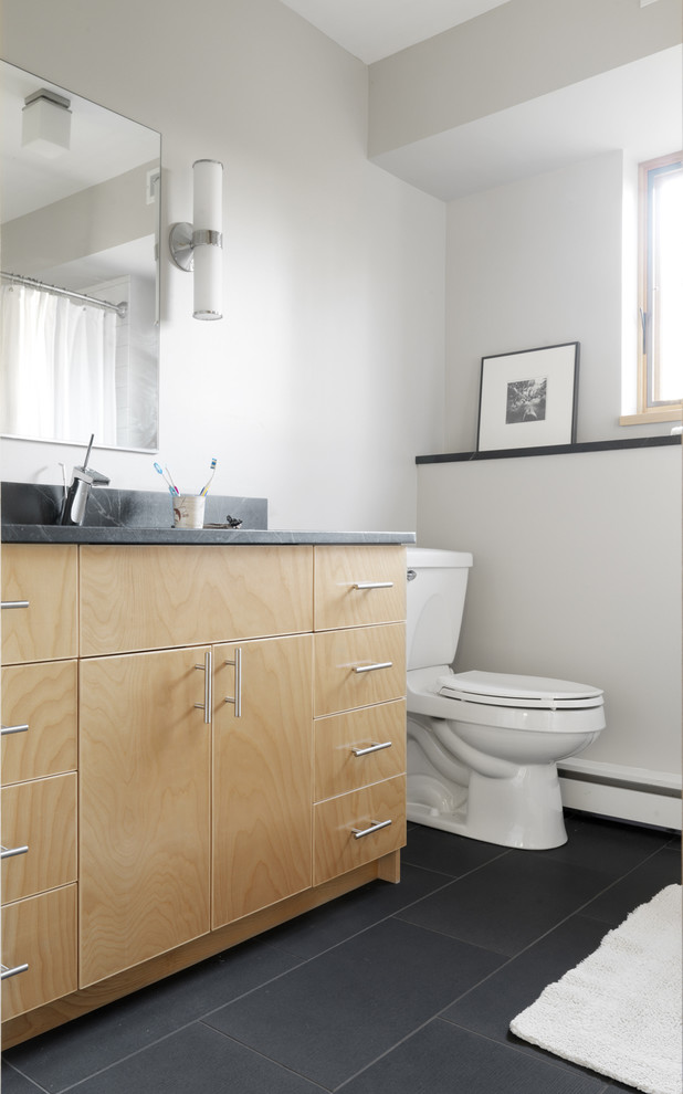 Modern inredning av ett badrum, med släta luckor, skåp i ljust trä, skiffergolv och svart golv