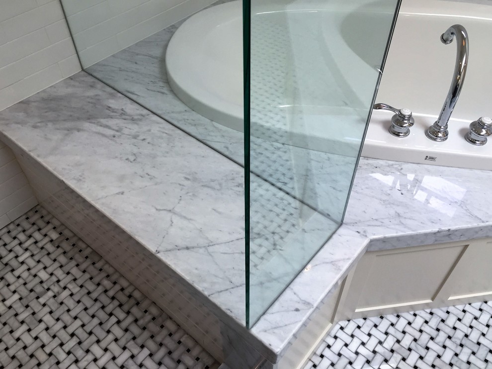 На фото: большая главная ванная комната в стиле неоклассика (современная классика) с черными фасадами, угловой ванной, угловым душем, белой плиткой, каменной плиткой, бежевыми стенами, полом из мозаичной плитки и мраморной столешницей