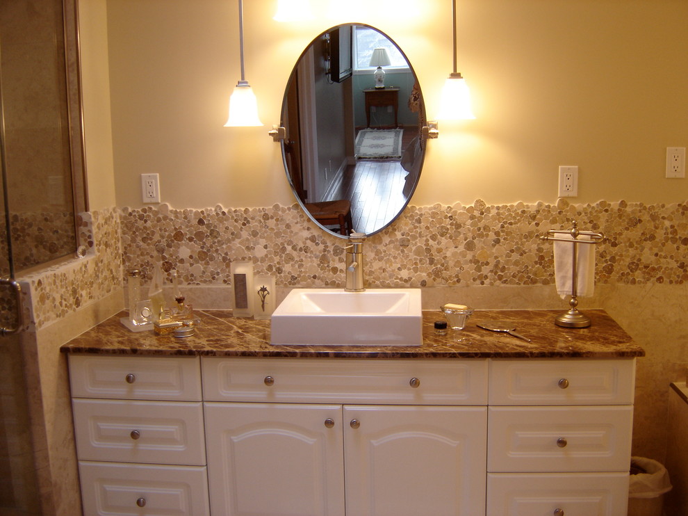 Klassisk inredning av ett badrum, med ett fristående handfat, luckor med upphöjd panel, vita skåp, marmorbänkskiva, ett badkar i en alkov, en dusch/badkar-kombination, en toalettstol med hel cisternkåpa och flerfärgad kakel