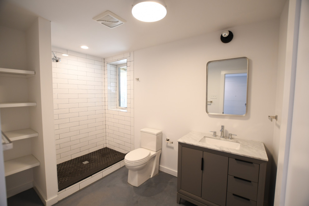 Inredning av ett 50 tals mellanstort grå grått badrum för barn, med släta luckor, grå skåp, en dusch i en alkov, en toalettstol med hel cisternkåpa, vita väggar, betonggolv, ett undermonterad handfat, marmorbänkskiva, grått golv och med dusch som är öppen