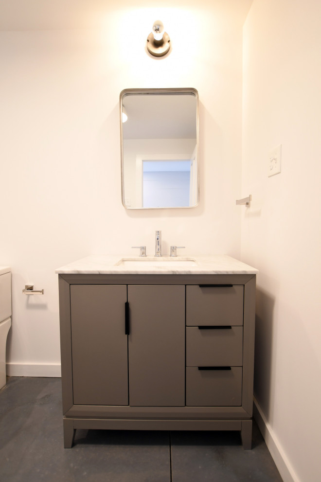 Mid-sized 1950s kids' concrete floor, gray floor and single-sink bathroom photo in New York with flat-panel cabinets, gray cabinets, a one-piece toilet, white walls, an undermount sink, marble countertops, gray countertops, a niche and a freestanding vanity