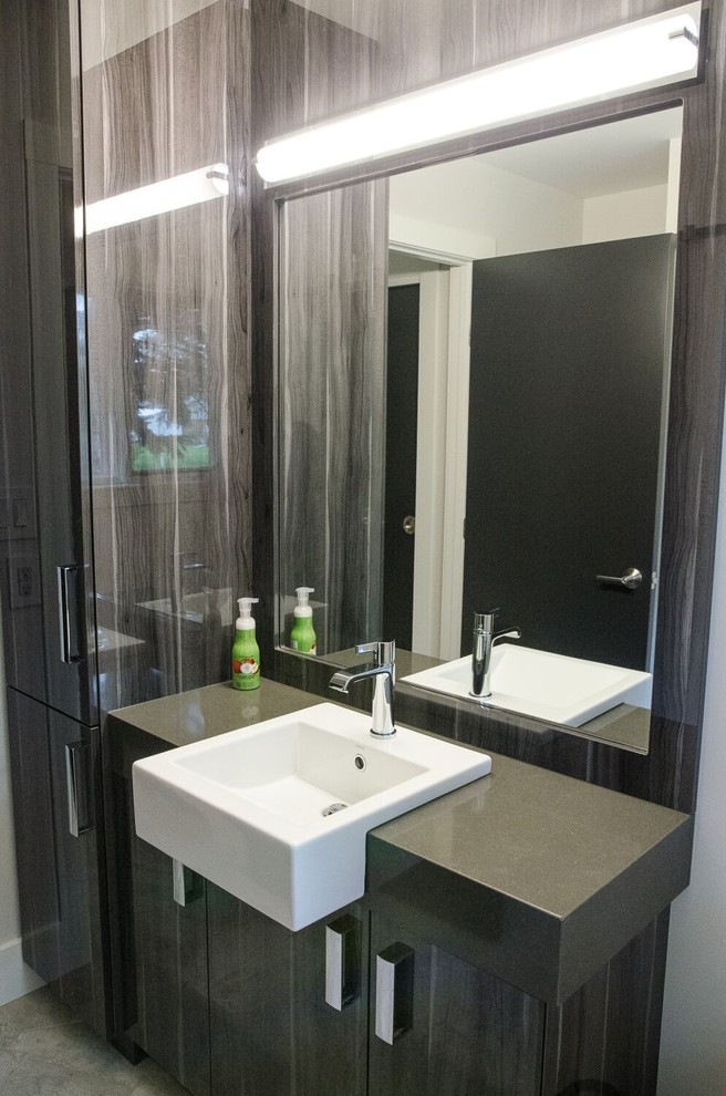 Diseño de cuarto de baño actual de tamaño medio con armarios con paneles lisos, puertas de armario negras, aseo y ducha, lavabo sobreencimera, encimera de cuarzo compacto, paredes grises y suelo de cemento