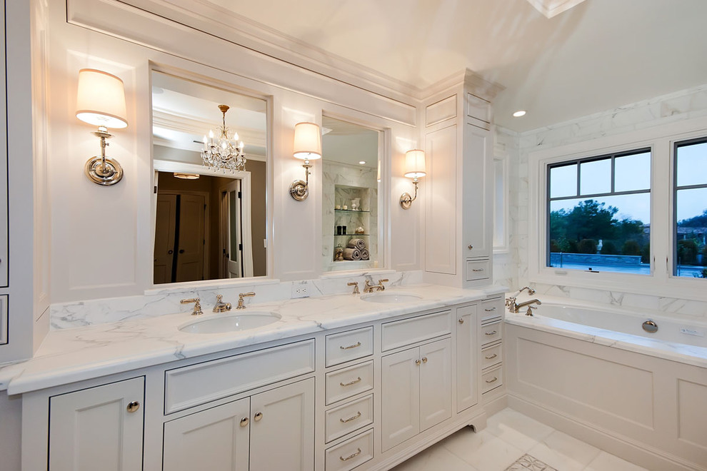 На фото: главная ванная комната в классическом стиле с фасадами в стиле шейкер, белыми фасадами, полновстраиваемой ванной, белой плиткой, врезной раковиной, мраморной столешницей, серыми стенами и мраморным полом с