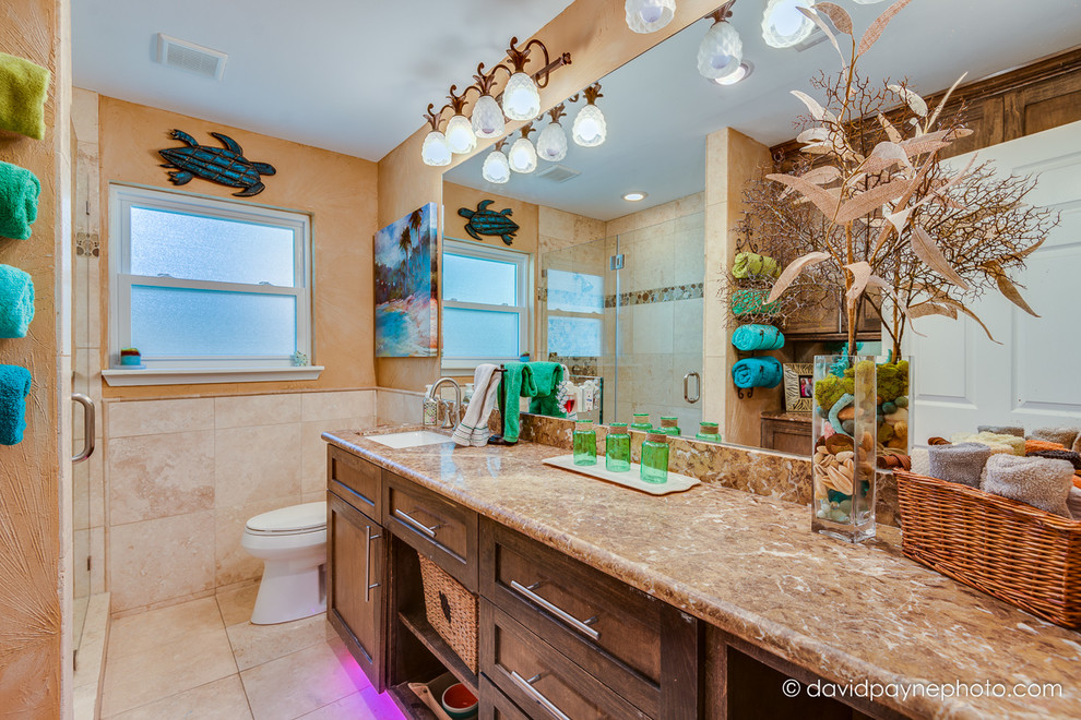 Inspiration for a small tropical kids' beige tile and stone tile travertine floor alcove shower remodel in Houston with a drop-in sink, shaker cabinets, dark wood cabinets, marble countertops, a one-piece toilet and orange walls