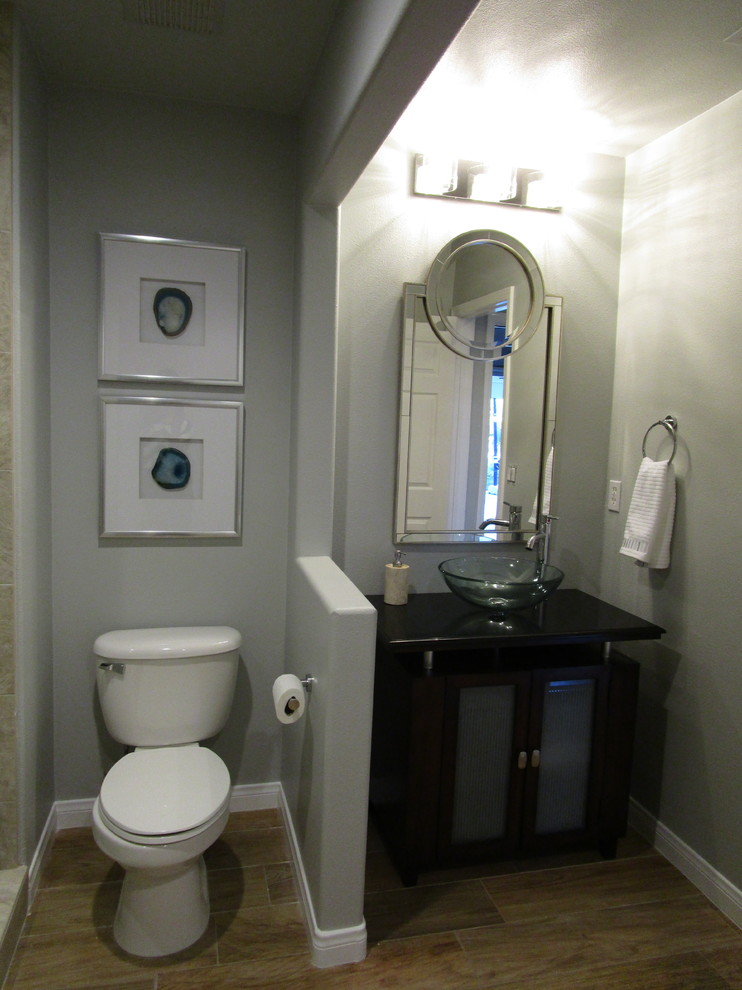 Klassisk inredning av ett mellanstort toalett, med skåp i mörkt trä, beige kakel, porslinskakel, klinkergolv i porslin, ett fristående handfat, granitbänkskiva, släta luckor, en toalettstol med separat cisternkåpa och grå väggar