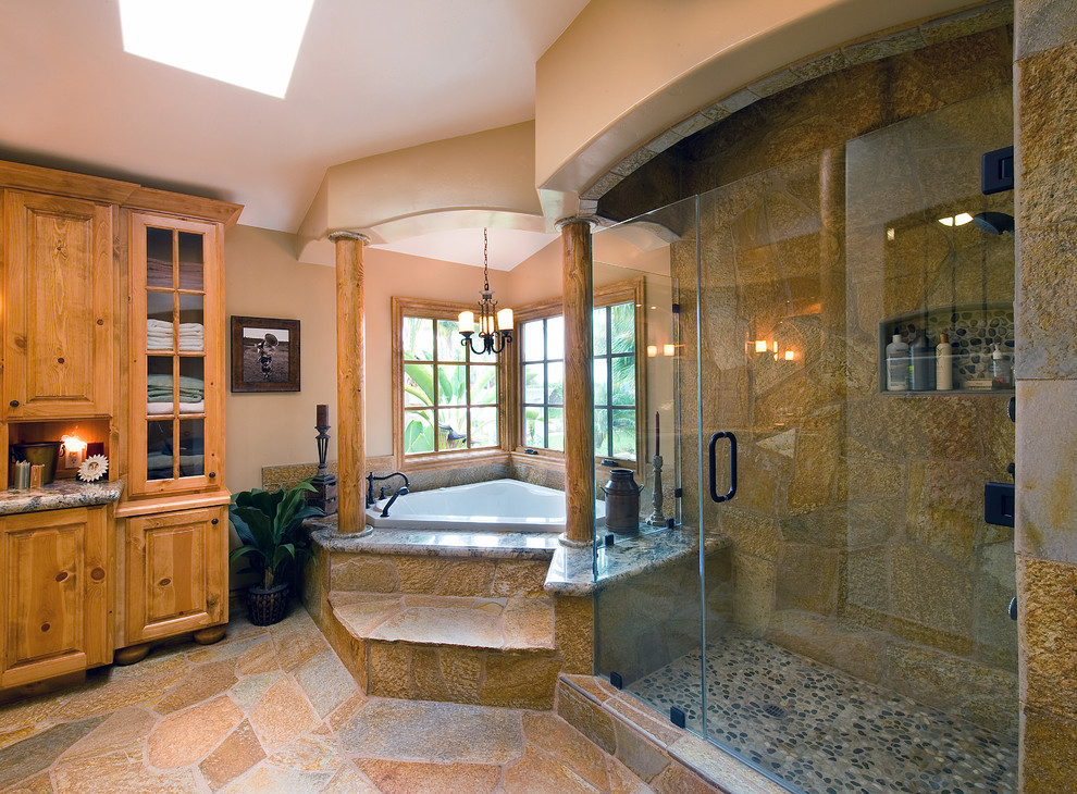 На фото: огромная ванная комната в стиле рустика с фасадами с выступающей филенкой, фасадами цвета дерева среднего тона, столешницей из гранита, угловой ванной, душем в нише, бежевыми стенами и полом из сланца с