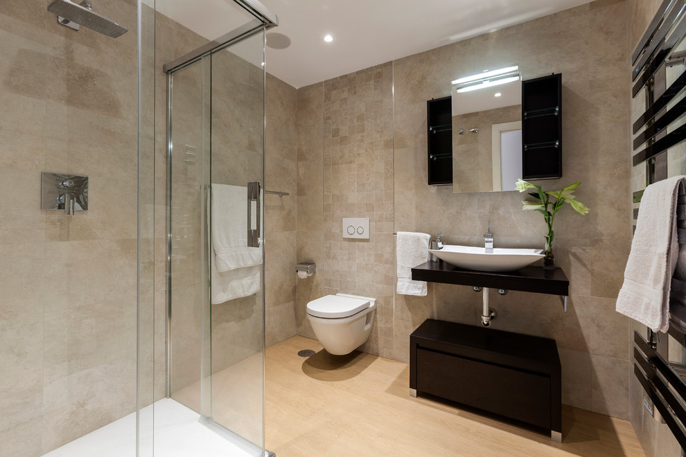 Cette image montre une salle d'eau design de taille moyenne avec un placard à porte plane, des portes de placard noires, une douche d'angle, WC suspendus, un sol en bois brun et une vasque.