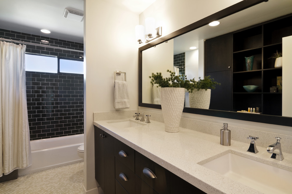 Modern inredning av ett badrum, med ett undermonterad handfat, släta luckor, svarta skåp, ett badkar i en alkov, en dusch/badkar-kombination, svart kakel och tunnelbanekakel