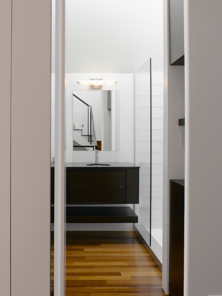 На фото: большая ванная комната в стиле модернизм с белыми стенами, темным паркетным полом, врезной раковиной, коричневым полом, открытым душем, плоскими фасадами, черными фасадами, душем в нише, белой плиткой, стеклянной плиткой, душевой кабиной и столешницей из искусственного камня