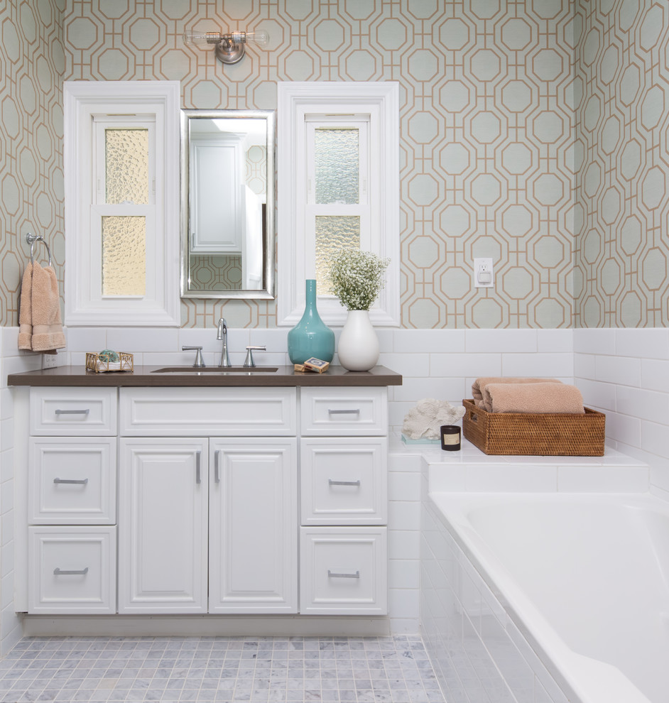 Cette image montre une salle de bain traditionnelle avec un placard à porte affleurante, des portes de placard blanches, une baignoire posée, un carrelage blanc, un carrelage métro, un mur multicolore, un lavabo encastré et une fenêtre.