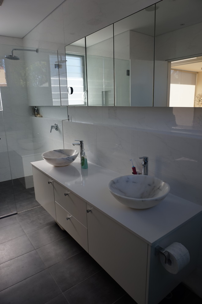 Modern inredning av ett mellanstort badrum, med ett fristående handfat, vita skåp, bänkskiva i kvarts, en dubbeldusch, en vägghängd toalettstol, vit kakel, keramikplattor, vita väggar och klinkergolv i porslin