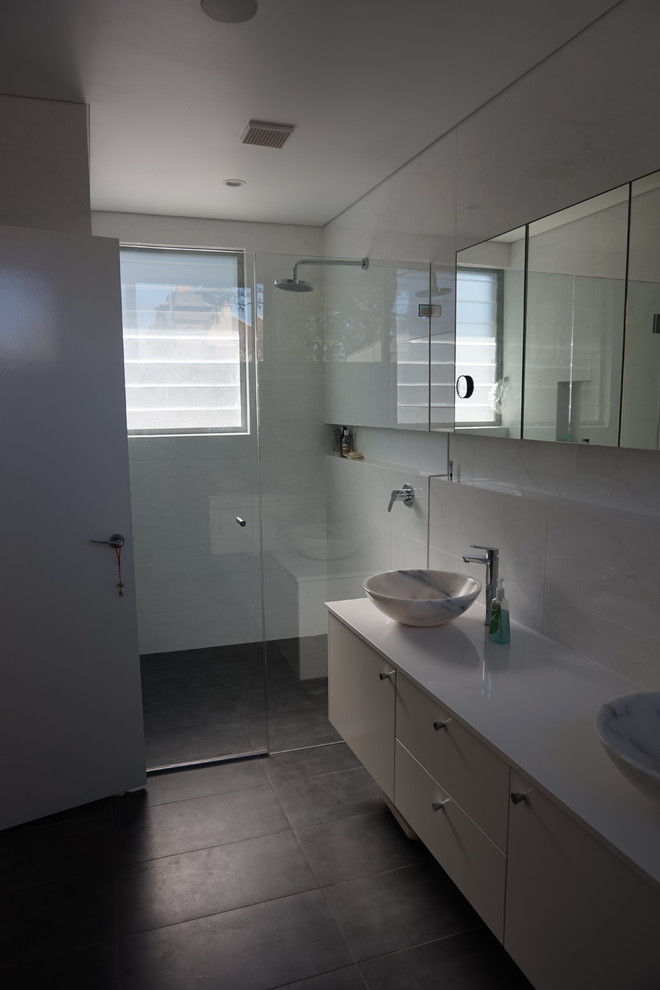 На фото: ванная комната среднего размера в стиле модернизм с настольной раковиной, белыми фасадами, столешницей из искусственного кварца, двойным душем, инсталляцией, белой плиткой, керамической плиткой, белыми стенами и полом из керамогранита