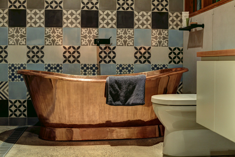 Mid-sized eclectic master blue tile and cement tile concrete floor bathroom photo in Sydney with light wood cabinets, a one-piece toilet, blue walls, a vessel sink and wood countertops