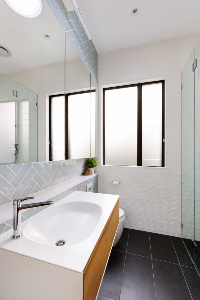 Modern inredning av ett mellanstort vit vitt badrum med dusch, med blå kakel, vit kakel, glaskakel, klinkergolv i keramik, ett integrerad handfat, bänkskiva i kvarts, svart golv, dusch med gångjärnsdörr, släta luckor, skåp i mellenmörkt trä och en dusch i en alkov
