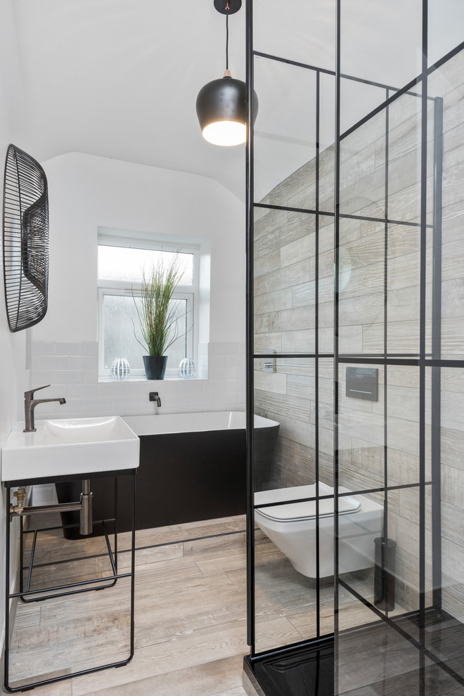 This is an example of a medium sized urban ensuite bathroom in West Midlands with a freestanding bath, a walk-in shower, a wall mounted toilet, white tiles, beige walls, porcelain flooring, a console sink, an open shower, metro tiles and beige floors.