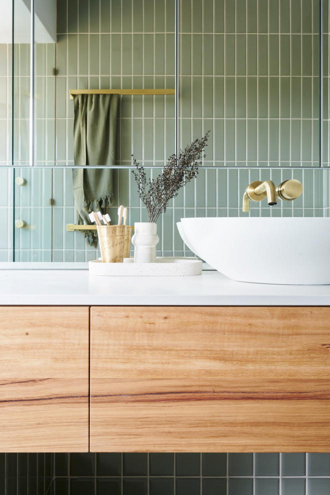 Пример оригинального дизайна: главная ванная комната среднего размера в современном стиле с фасадами островного типа, фасадами цвета дерева среднего тона, отдельно стоящей ванной, душевой комнатой, унитазом-моноблоком, зеленой плиткой, удлиненной плиткой, зелеными стенами, полом из керамической плитки, настольной раковиной, столешницей из искусственного кварца, серым полом, открытым душем и белой столешницей