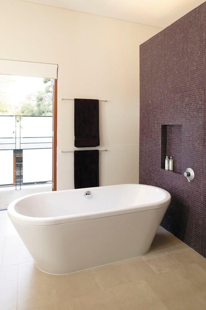 Immagine di una stanza da bagno minimal con vasca freestanding, piastrelle di vetro e pavimento in travertino